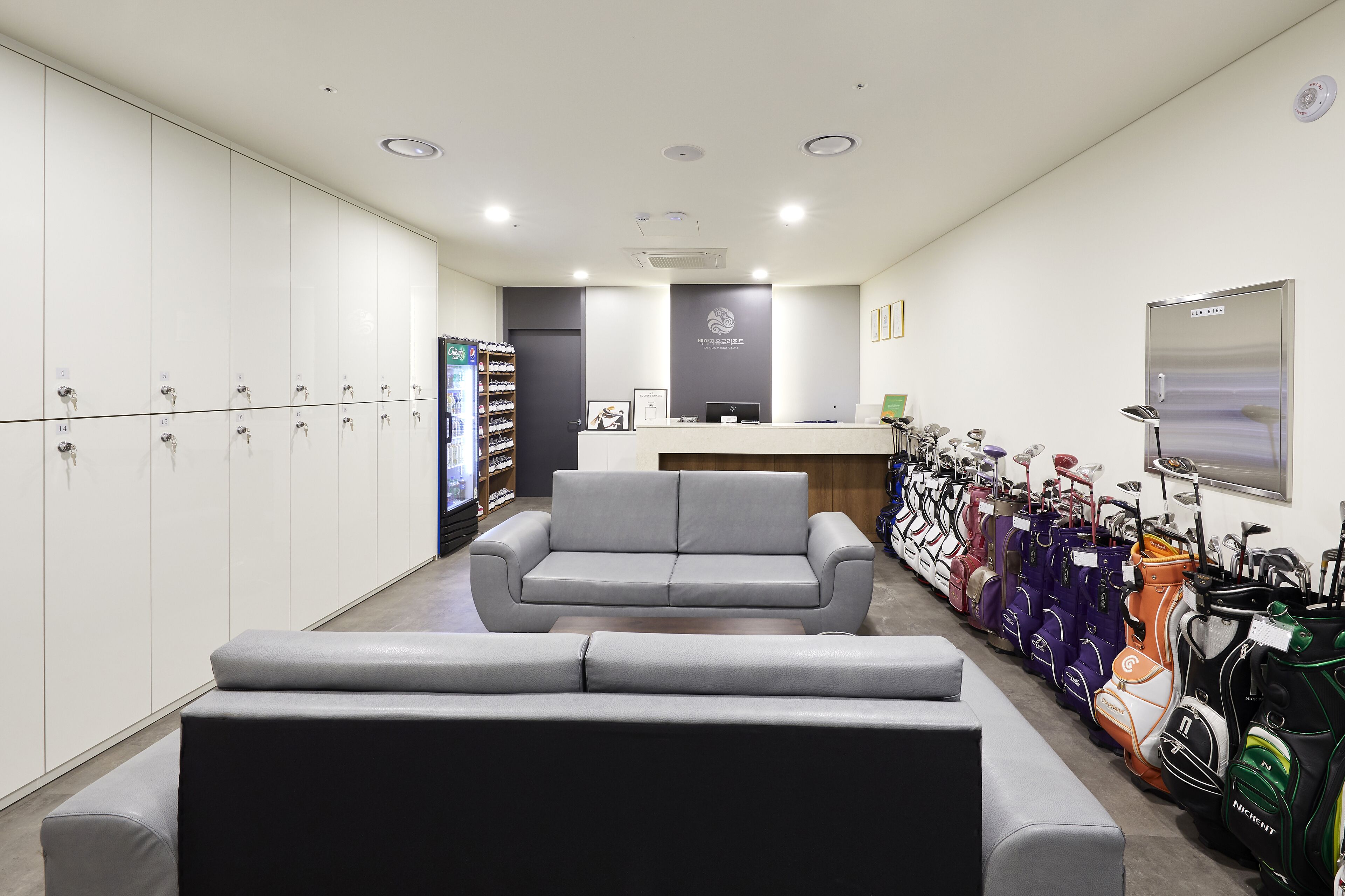 A reception area with a grey sofa, a reception desk, and a row of golf bags.