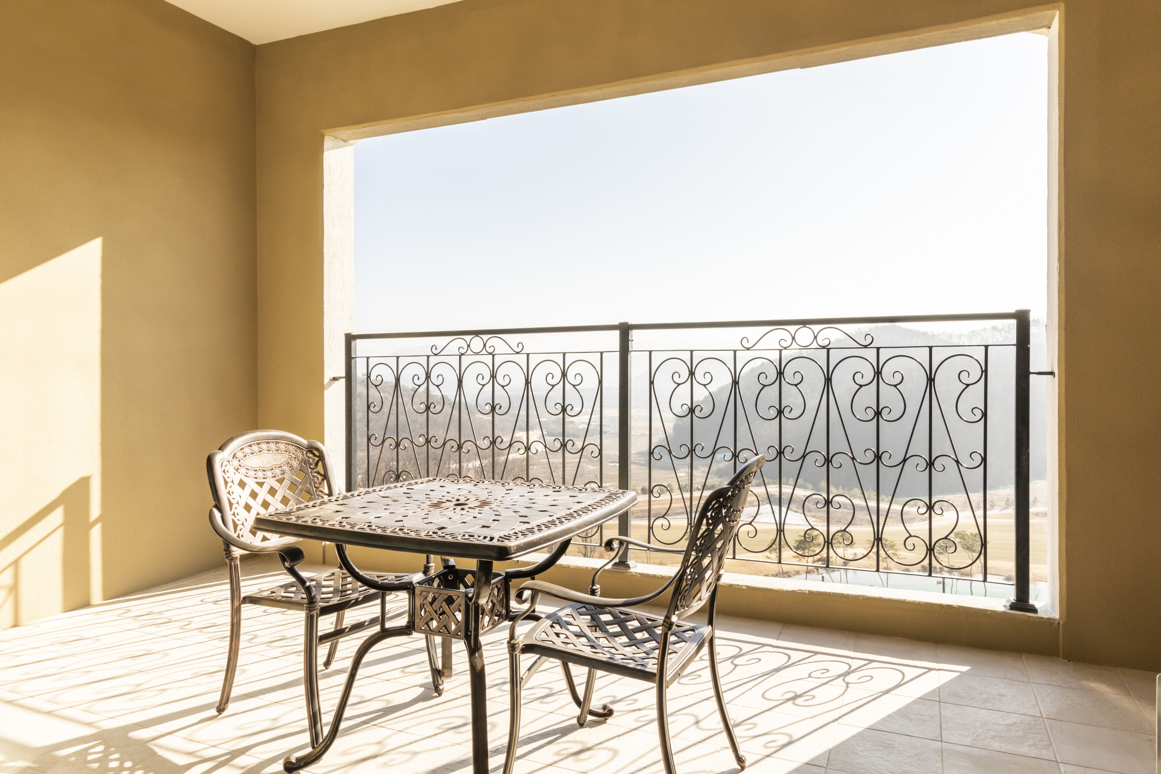 A balcony with a table and chairs, a wrought iron railing, and a view of the landscape.