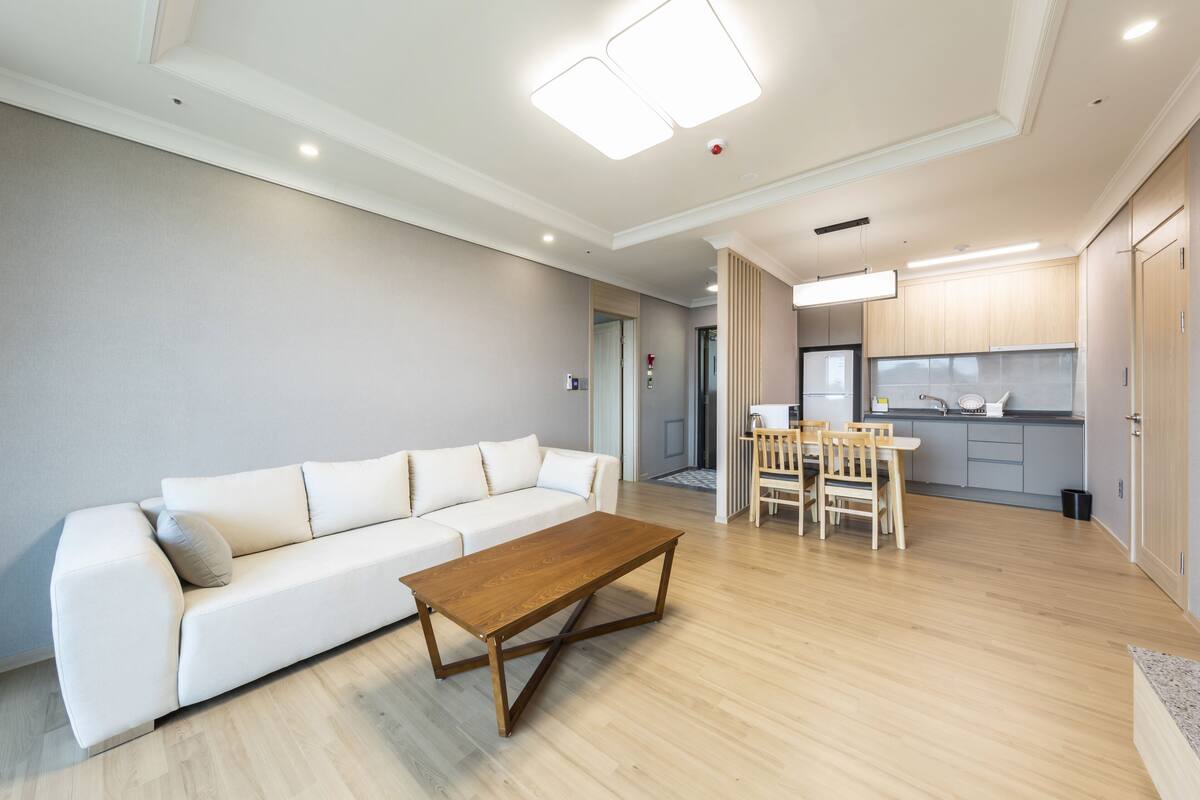 A modern living room with a white sofa, wooden coffee table, and a dining area with chairs and a table.