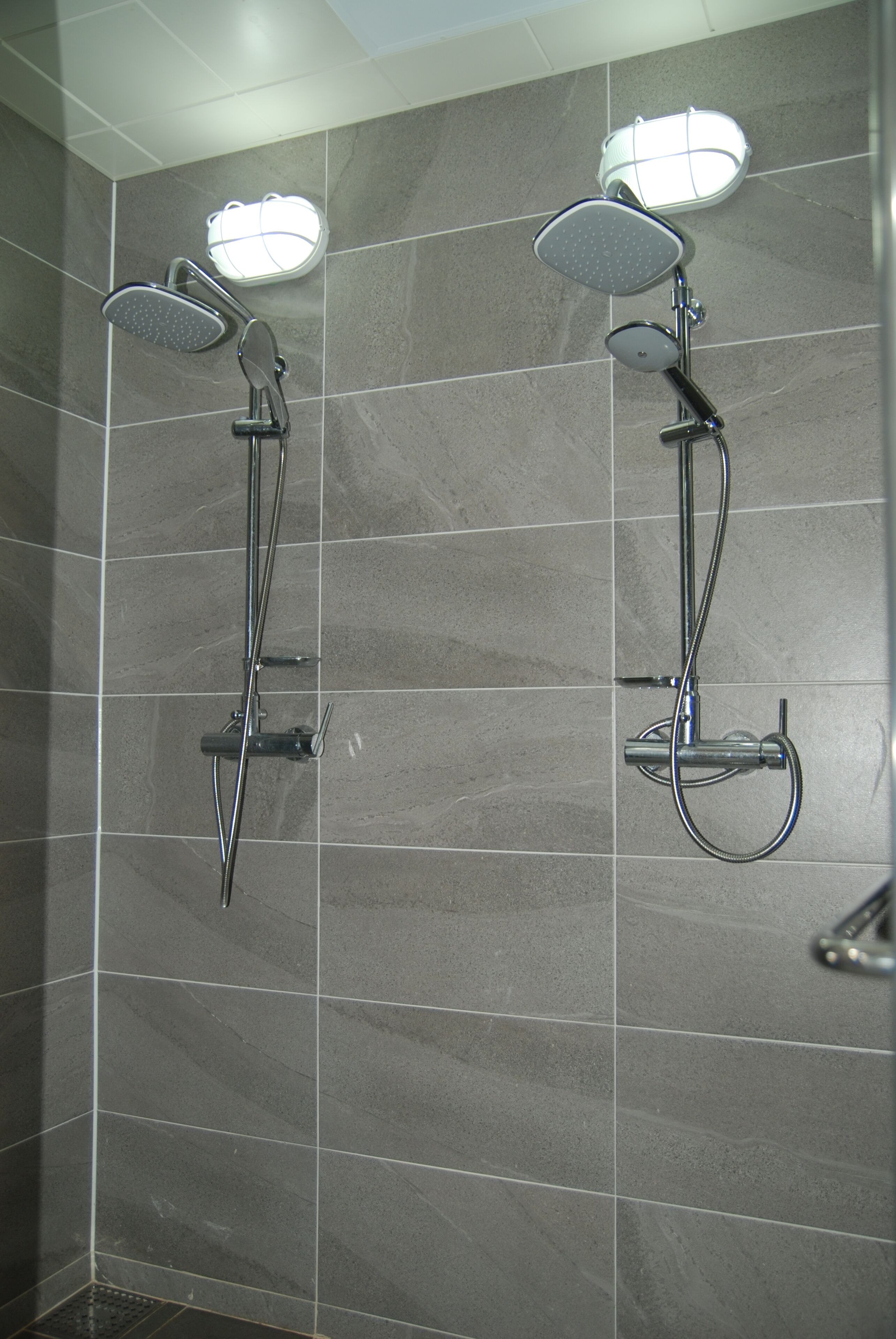 A shower area with two showerheads and a light fixture.