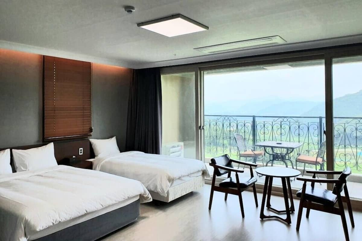 A hotel room with two beds, a balcony with a table and chairs, and a view of the mountains.