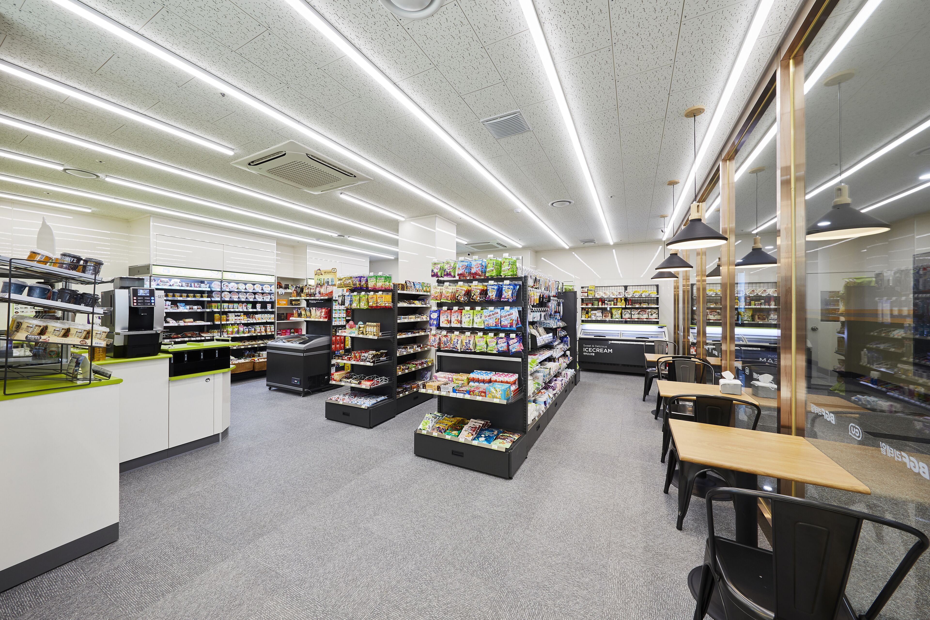 A modern supermarket interior with wide aisles, refrigerated sections, and a seating area.