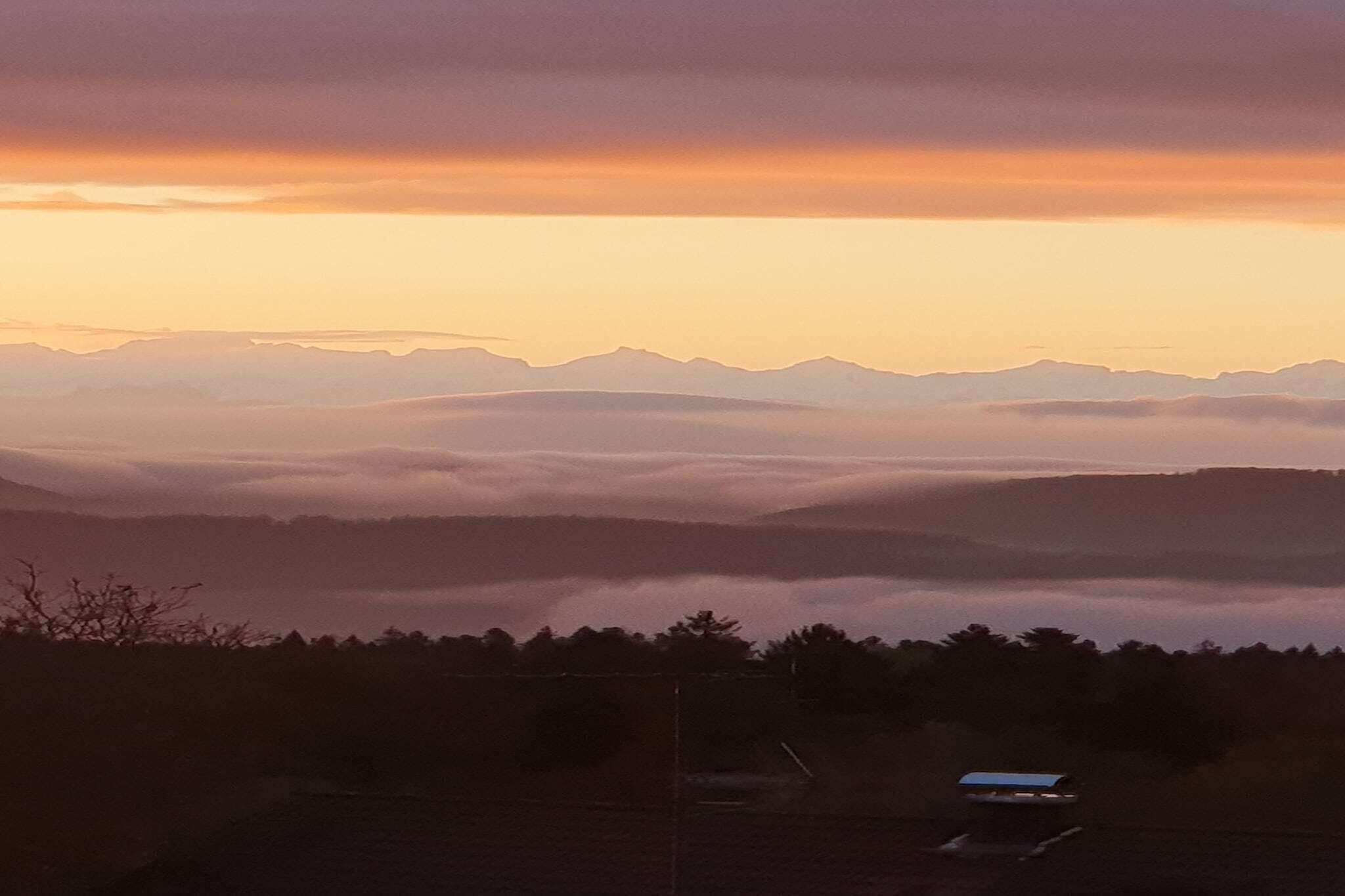 Paisagem montanhosa com céu claro e um pequeno edifício em primeiro plano.