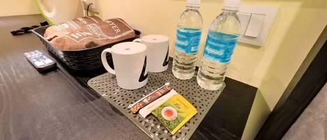 A tray with a towel, two mugs, two bottles of water, a remote control, and a card on a hotel table.