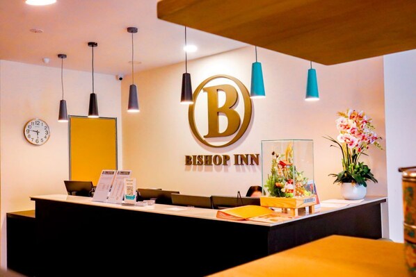 Un comptoir d’accueil à l’hôtel Bishop Inn, orné d’un grand logo en forme de « B », d’une horloge et d’un arrangement floral.
