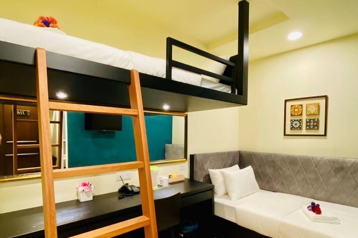 A bunk bed with a desk and chair, a sofa, a wooden ladder, and a mirror.