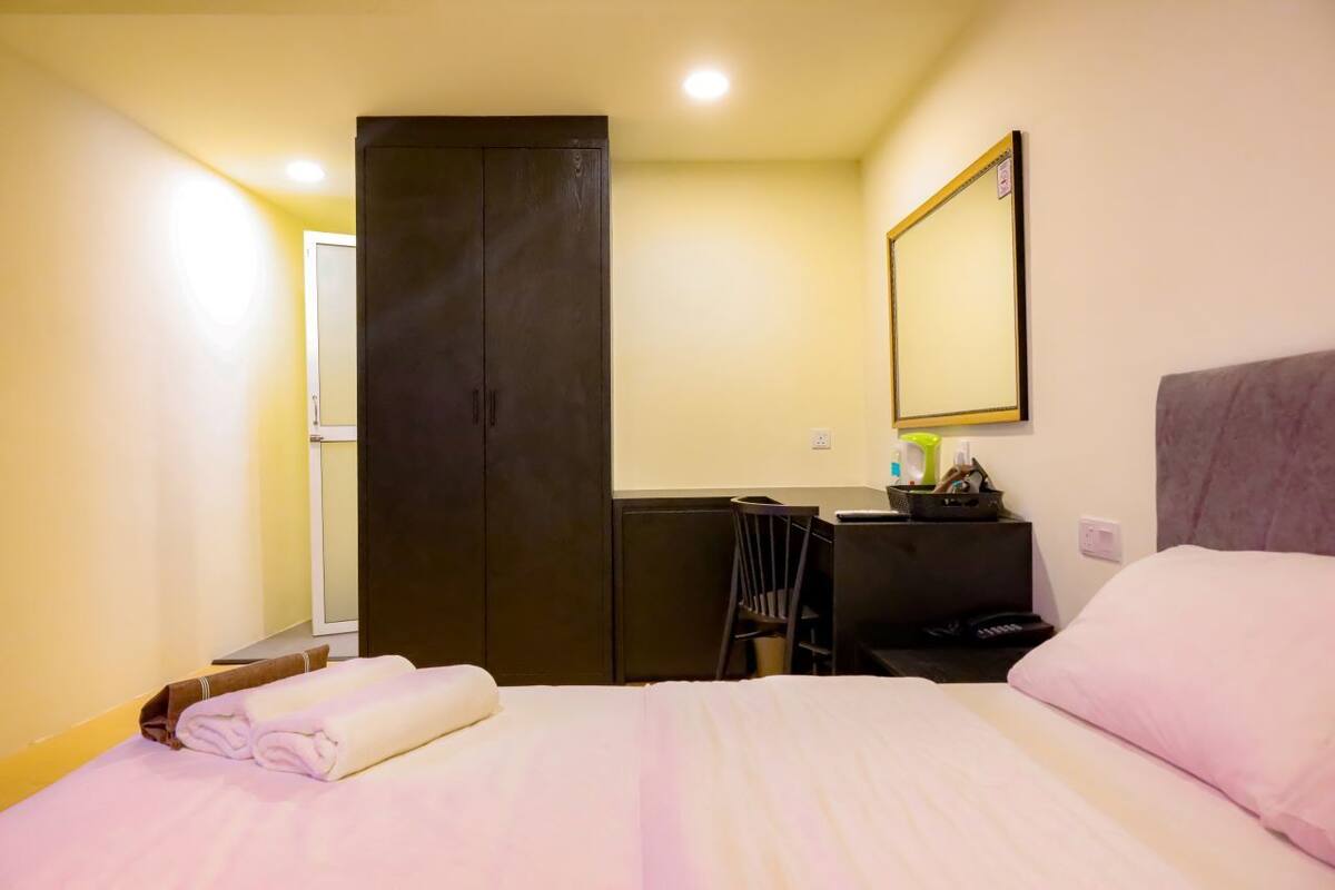 A hotel room with a bed, a desk, a chair, a wardrobe, and a mirror.