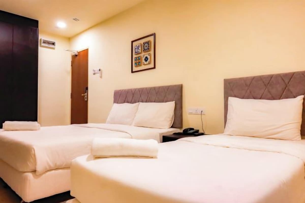 A hotel room with two beds, a bedside table with a phone, and a wall-mounted picture.