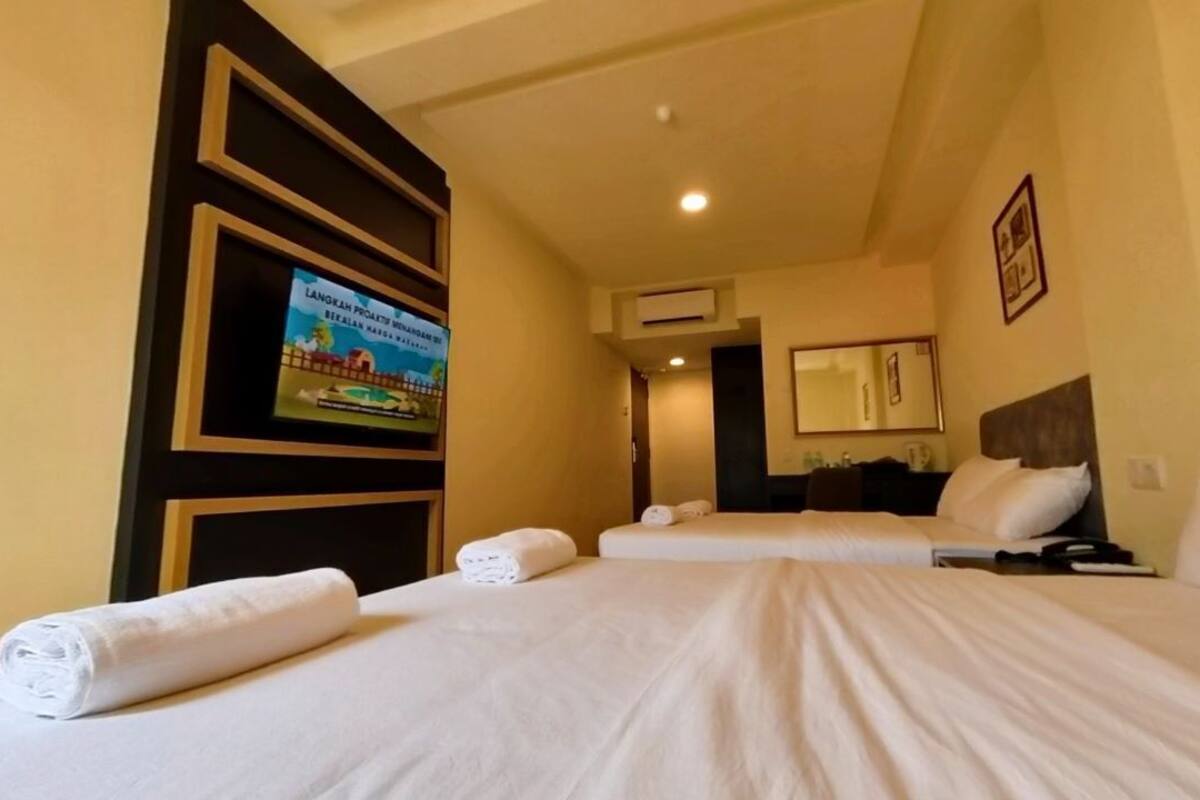 A hotel room with two beds, a television on the wall, and a framed picture.