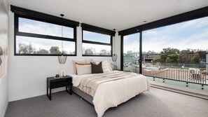 Une chambre avec un grand lit, une table de chevet et une vue sur le paysage urbain, grâce à de grandes fenêtres.