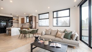 A modern living room with a sofa, coffee table, and a dining area with chairs and a table. - Pet Friendly - Sport Precinct Luxury Style over four levels (Cremorne)
