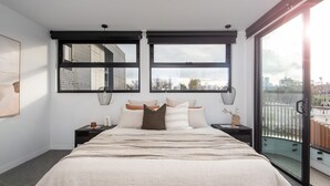 A modern bedroom with a large bed, two windows, and a view of the city. - Pet Friendly - Sport Precinct Luxury Style over four levels (Cremorne)