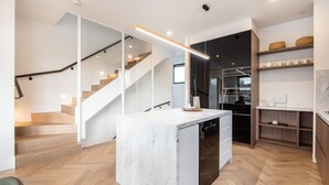 A modern kitchen with a marble island, wooden flooring, and a staircase with glass railings. - Pet Friendly - Sport Precinct Luxury Style over four levels (Cremorne)
