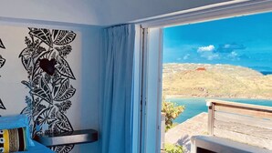 Un dormitorio con un ventanal grande, una cama, una mesita de noche y vistas a un paisaje costero.