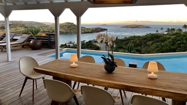 Una terraza de madera con piscina, sillas de descanso y una mesa con lámparas.