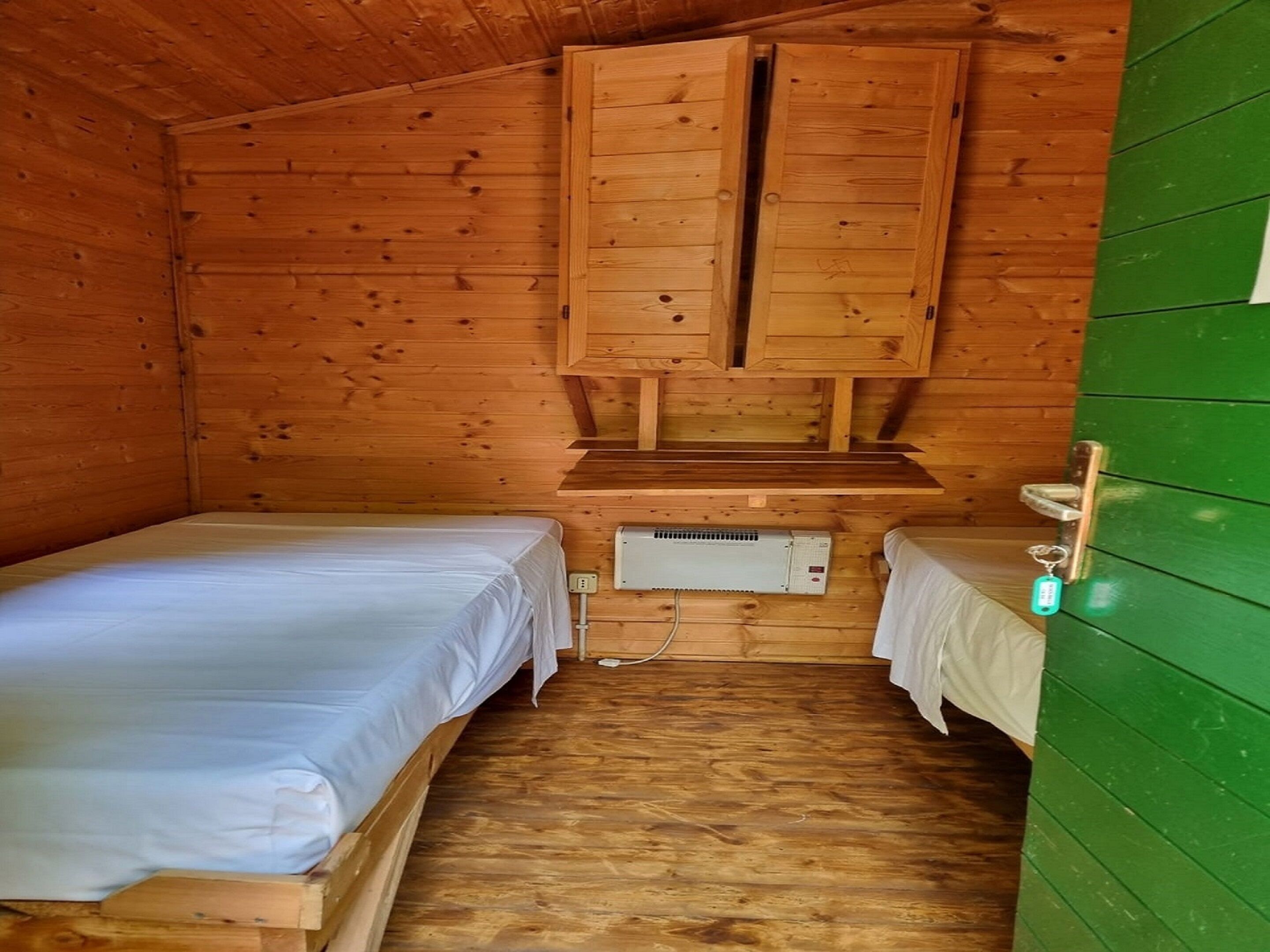 Une petite cabane avec deux lits en bois, un placard intégré et un mur vert.