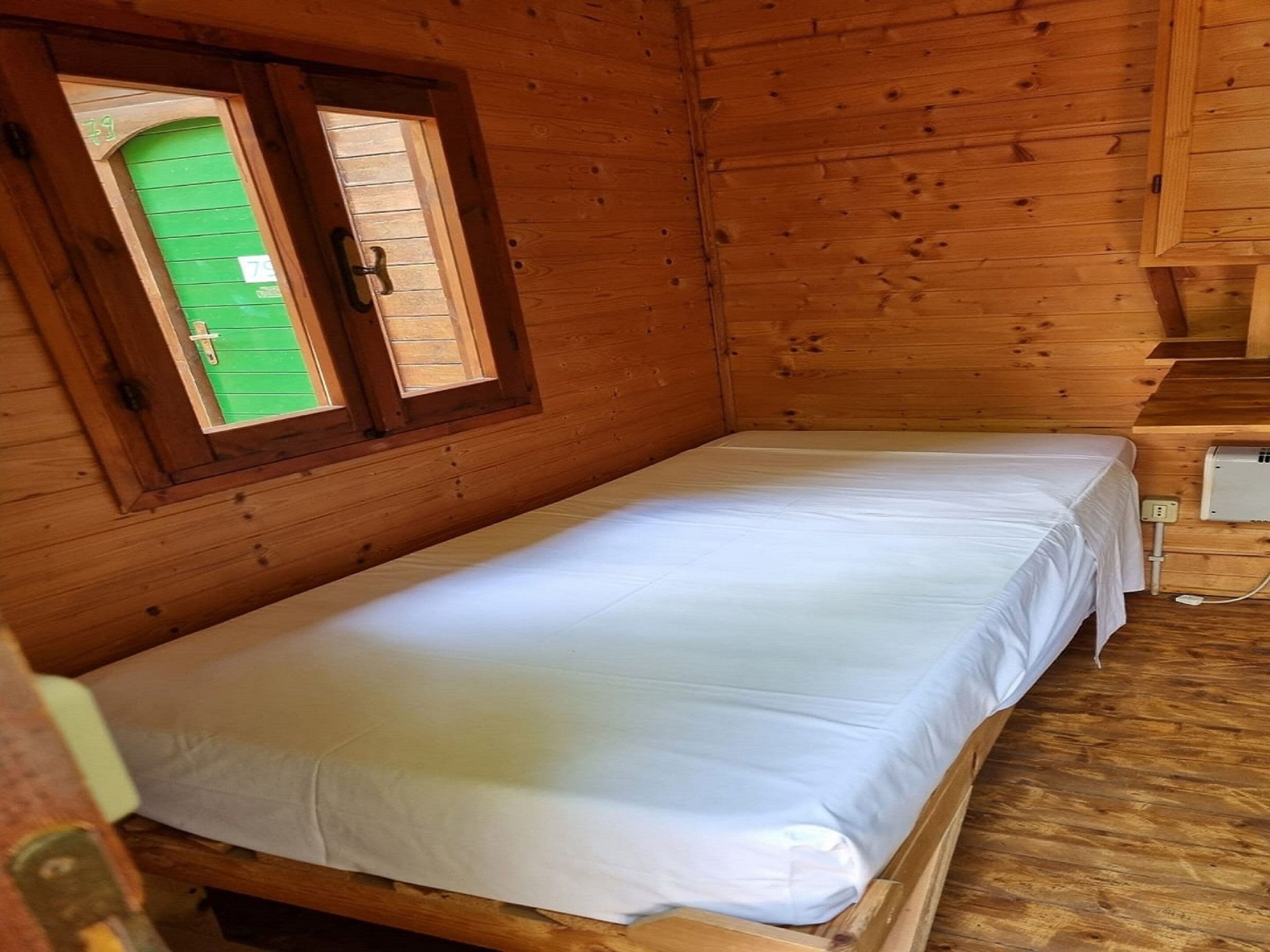 A single wooden bed in a cabin-style room with a green door and a window.