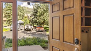 Puerta de madera que da a un estacionamiento con vehículos, rodeado de vegetación y un paisaje montañoso.