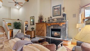 Una sala de estar acogedora con chimenea de piedra, asientos cómodos y una escalera que sube a otro nivel.