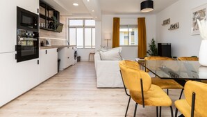 A modern kitchen with built-in appliances, a dining area with yellow chairs, and a living space with a sofa and a TV. - Nala Apartment, Wifi, Algarve !new! (Faro)