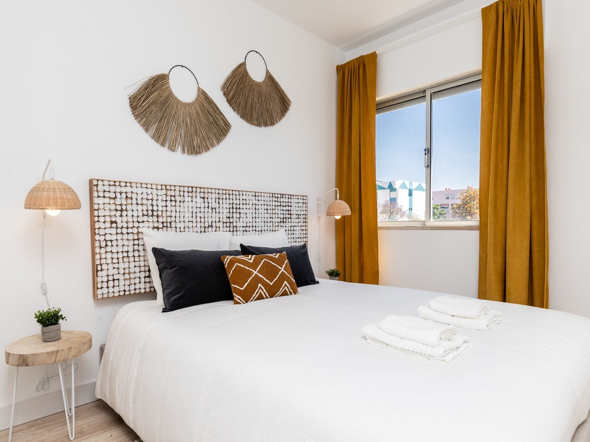 A modern hotel room with a large bed, two wall-mounted lamps, a decorative headboard, and a window with curtains.