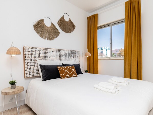 A modern hotel room with a large bed, two wall-mounted lamps, a decorative headboard, and a window with curtains. - Nala Apartment, Wifi, Algarve !new! (Faro)
