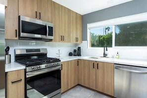 Une cuisine moderne dotée d’appareils électroménagers en acier inoxydable, de meubles en bois et d’une fenêtre donnant sur un paysage verdoyant.