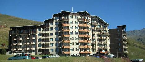 A multi-story hotel with balconies, located in a hilly area with clear skies.