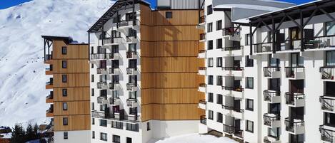A modern multi-story hotel with balconies, situated in a snowy mountainous area.