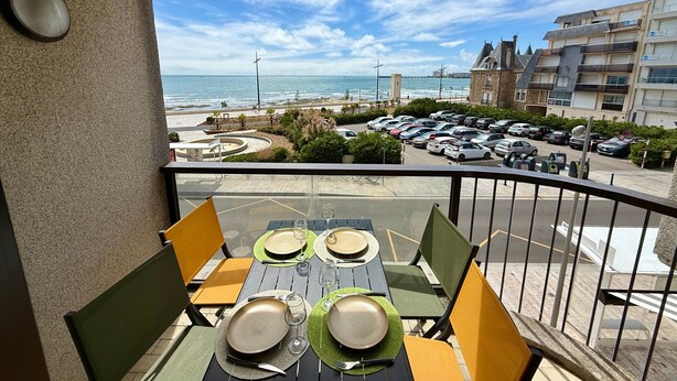 Ein Balkon mit Tisch für vier Personen, mit Blick auf einen Strand und einen Parkplatz.