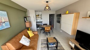 Ein Wohnzimmer mit Sofa, Couchtisch, Fernseher und einem Essbereich mit Stühlen und Tisch.