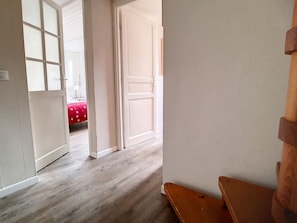 A hallway with wooden flooring, white walls, and a partially open door leading to a room with a red bedspread. - Spacious Duplex Near Slopes · 3 Bedrooms · 2 Balconies (Les Menuires)