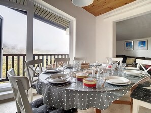 A dining area with a round table set for four, large windows, and a view of a mountainous landscape. - Spacious Duplex Near Slopes · 3 Bedrooms · 2 Balconies (Les Menuires)