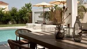 A poolside area with lounge chairs, umbrellas, and a table with decorative vases. - Anthis Luxury Villa (Zakynthos)
