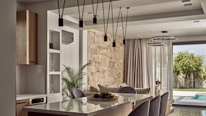 A modern kitchen with a central island, bar stools, pendant lighting, and a stone accent wall. - Anthis Luxury Villa (Zakynthos)