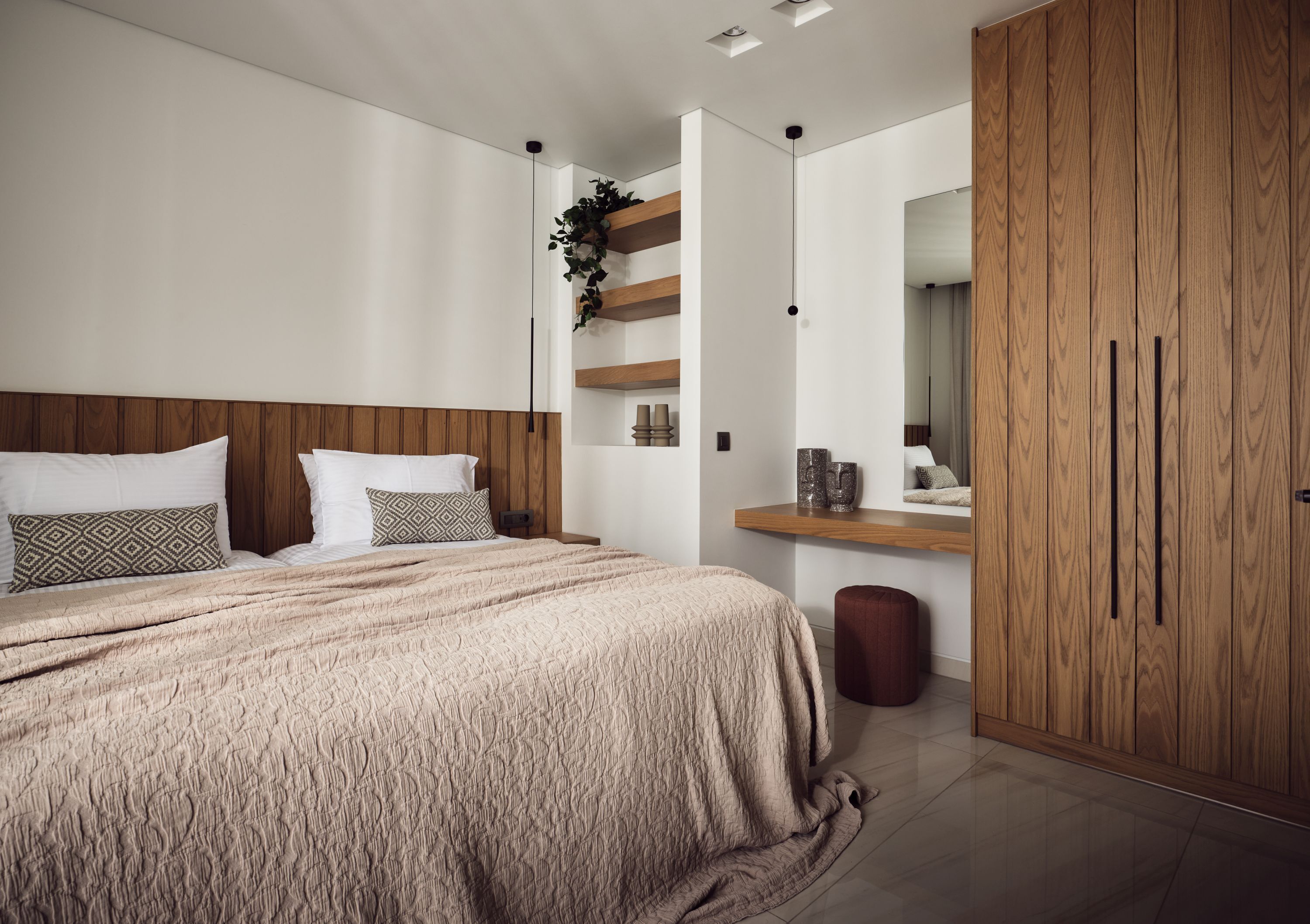Un dormitorio moderno con una cama grande, cabecera de madera, un armario de madera, una planta pequeña y un espejo sobre el tocador.