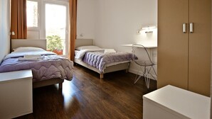 A bedroom with two beds, a desk, and a wardrobe.