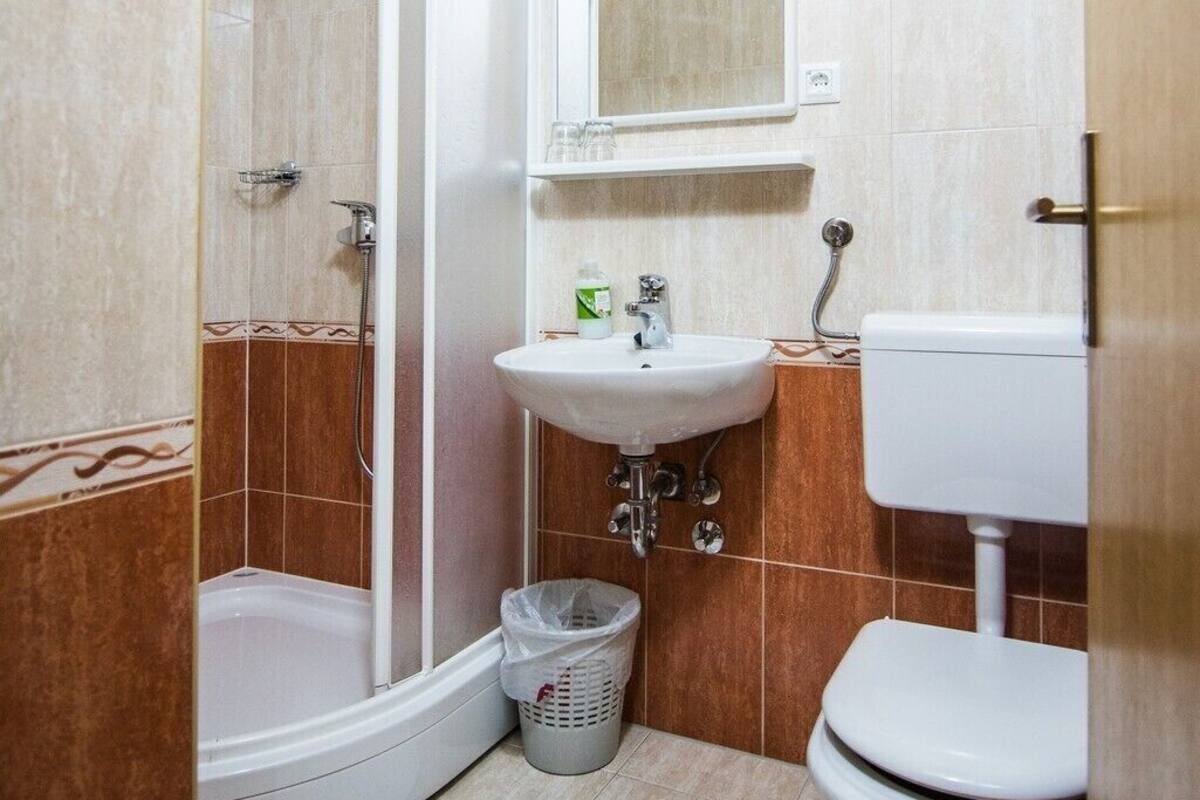 A bathroom with a shower, sink, toilet, and a small rug.