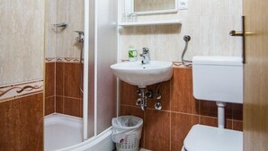 A bathroom with a shower, sink, toilet, and a small rug.