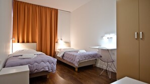 A hotel room with two beds, a desk, and a wardrobe.