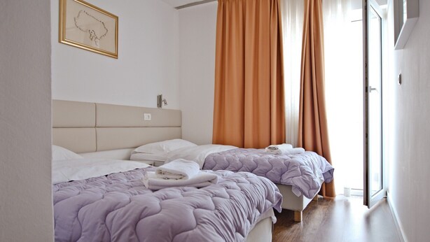 A hotel room with two beds, a headboard, a bedside table, and a window with curtains.