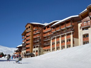 A multi-story hotel with balconies and ski slopes in the background.