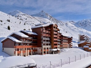 A multi-story hotel with balconies, set against a snowy mountain backdrop.