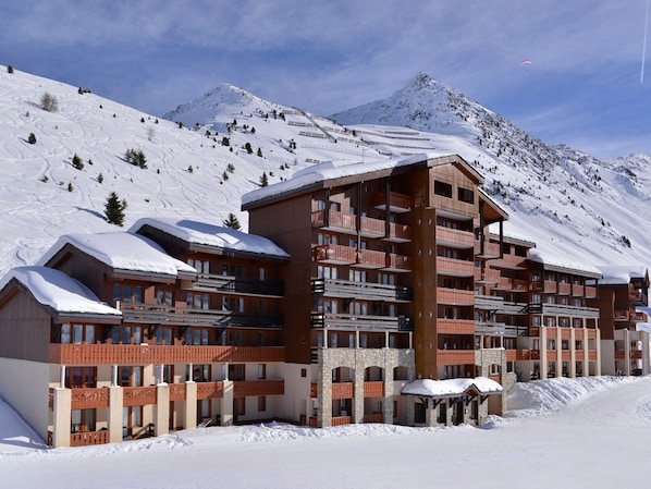 A multi-story hotel with balconies, set against a snowy mountain backdrop.