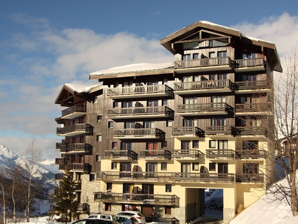 Un hôtel à plusieurs étages, doté de balcons, d’une base en pierre et offrant une vue sur les pistes de ski.