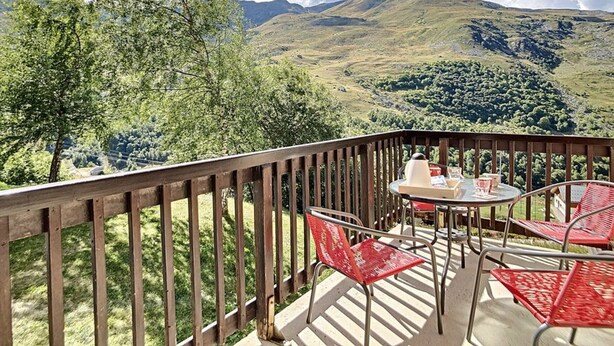 Un balcone con tavolo e sedie, affacciato su un paesaggio montuoso.
