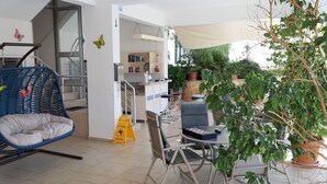 A modern living room with a blue hanging chair, a dining table with chairs, and a bookshelf. - Oase Apart (Kalkan)