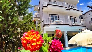 A modern two-story building with a pool, surrounded by lush greenery and vibrant flowers. - Oase Apart (Kalkan)