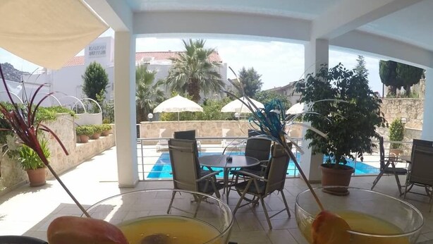 Two martini glasses with a yellow drink on a table in a covered outdoor area with a pool and chairs in the background. - Oase Apart (Kalkan)