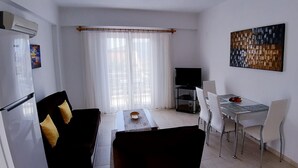 A compact living space with a dining area, a sofa with decorative pillows, a TV, and a painting on the wall. - Oase Apart (Kalkan)